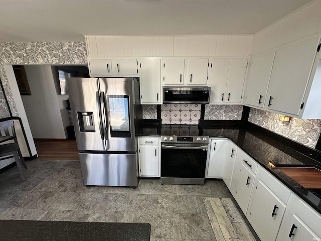 kitchen featuring appliances with stainless steel finishes, dark stone counters, white cabinets, and wallpapered walls