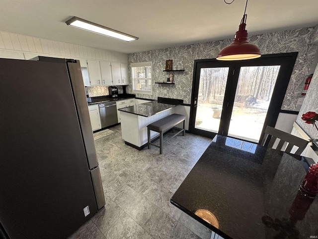 kitchen featuring pendant lighting, stainless steel appliances, dark countertops, white cabinetry, and wallpapered walls