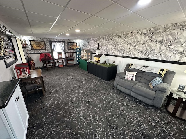 living room with a paneled ceiling, wallpapered walls, dark colored carpet, and wainscoting