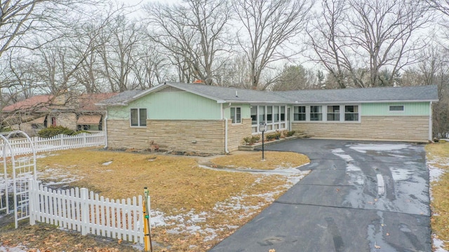 single story home featuring stone siding, driveway, and fence