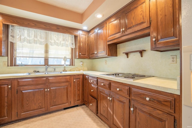 kitchen featuring brown cabinets, light countertops, stainless steel gas stovetop, and a sink