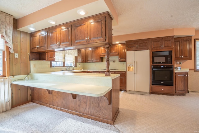 kitchen with a peninsula, a kitchen breakfast bar, light countertops, black appliances, and brown cabinetry