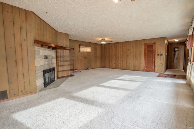 unfurnished living room featuring wooden walls, ceiling fan, a textured ceiling, carpet floors, and a fireplace