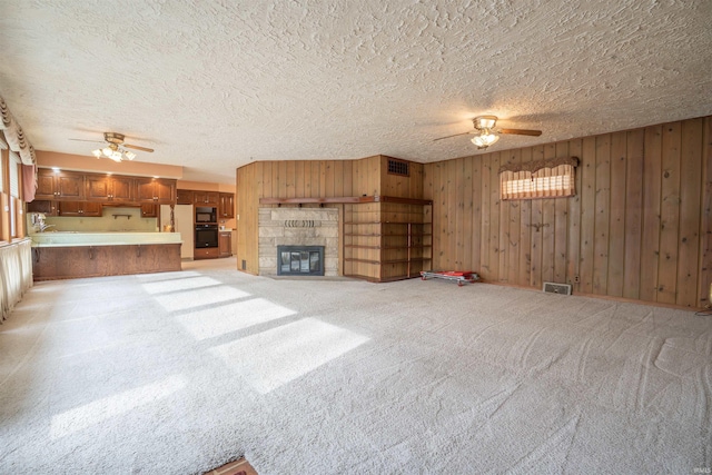 unfurnished living room with visible vents, a fireplace, light carpet, and ceiling fan