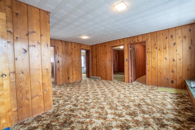 spare room featuring carpet floors, wood walls, and visible vents