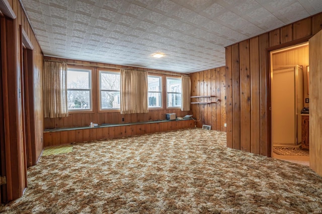 carpeted empty room with visible vents and wood walls