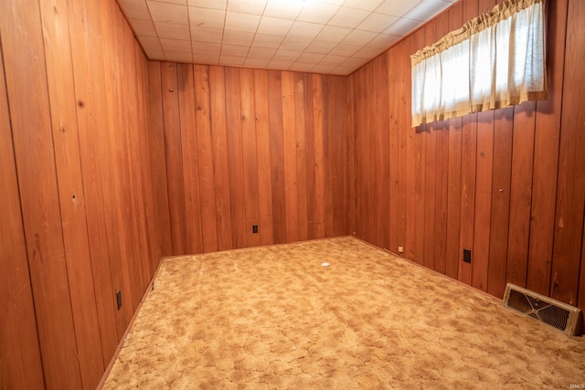 carpeted spare room with wooden walls and visible vents