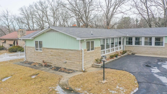 ranch-style home featuring a shingled roof, stone siding, and driveway