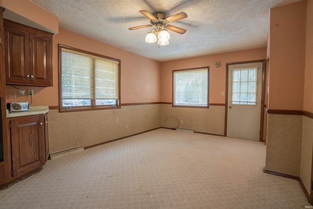 unfurnished room featuring light carpet, a wainscoted wall, baseboard heating, and a textured ceiling