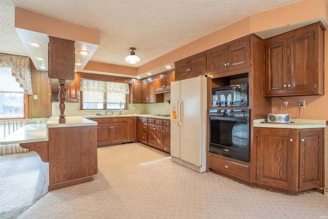 kitchen featuring a peninsula, black appliances, light countertops, and brown cabinetry