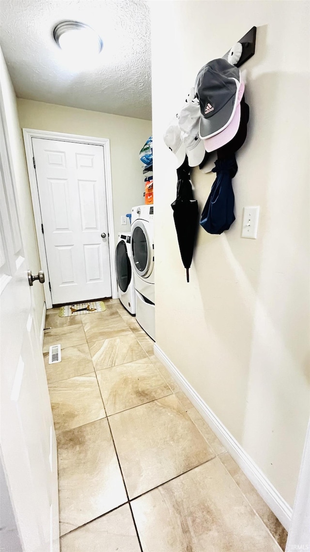 laundry area with washing machine and clothes dryer, visible vents, a textured ceiling, laundry area, and baseboards