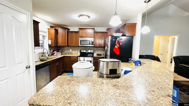 kitchen with a sink, appliances with stainless steel finishes, decorative backsplash, a center island, and decorative light fixtures