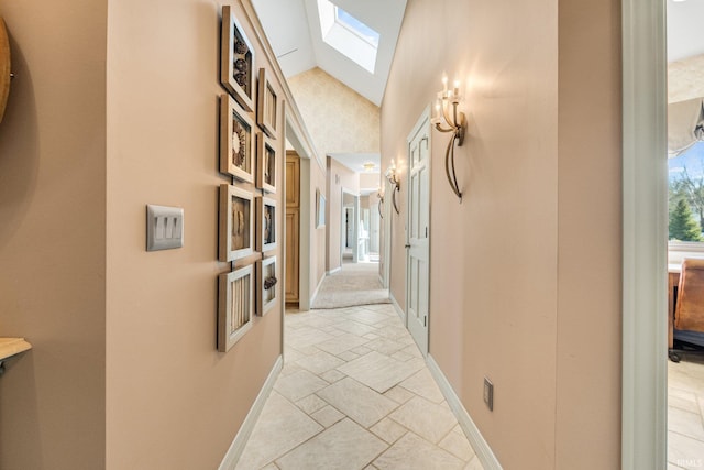 hallway featuring vaulted ceiling with skylight, baseboards, and stone finish flooring