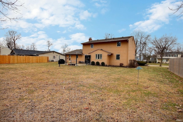 rear view of house featuring a chimney, fence, and a lawn