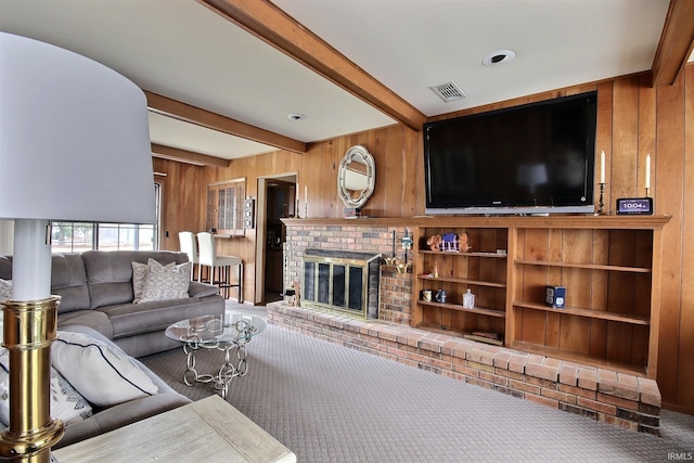 carpeted living area with beam ceiling, visible vents, a fireplace, and wooden walls