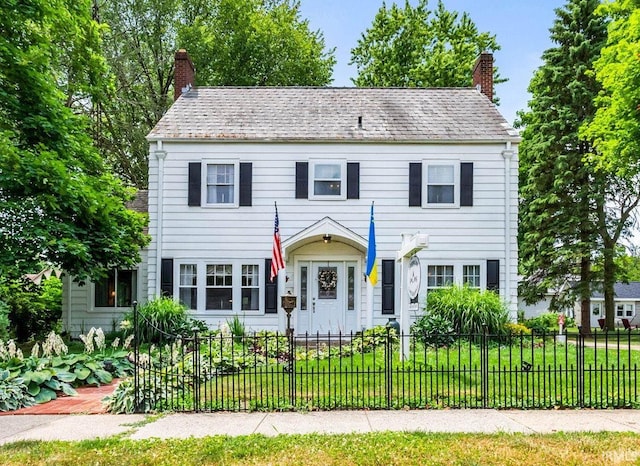 colonial home featuring a fenced front yard, a chimney, and a front yard