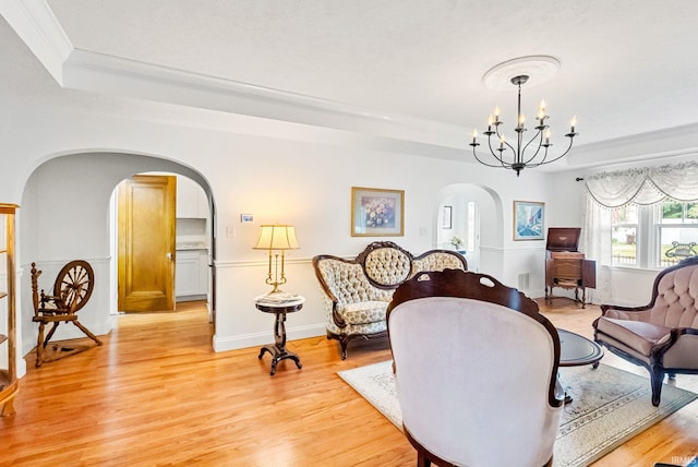 living area featuring arched walkways, a chandelier, light wood-style floors, ornamental molding, and a raised ceiling