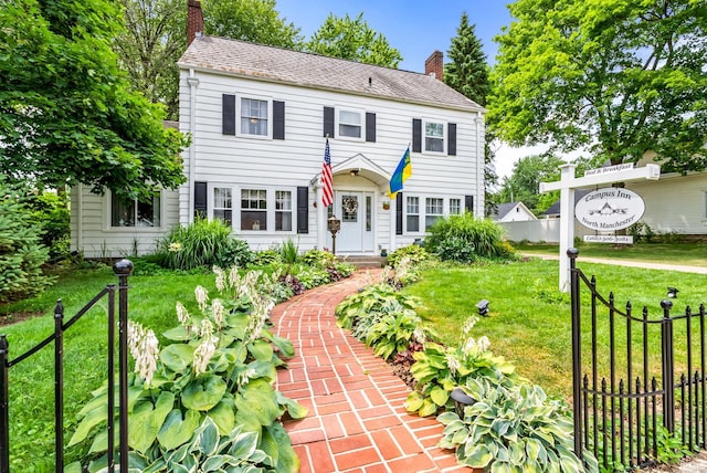 colonial home featuring a chimney, fence, and a front yard