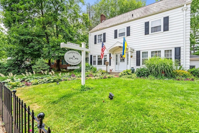 colonial-style house with a chimney, fence, and a front lawn