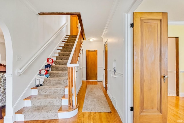 stairs with arched walkways, crown molding, visible vents, wood finished floors, and baseboards