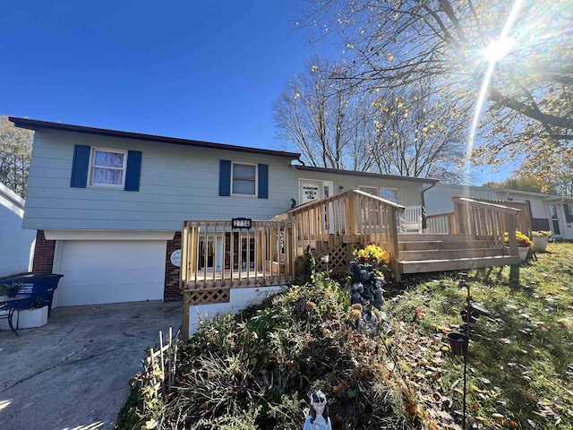 rear view of house featuring an attached garage, brick siding, driveway, and a wooden deck