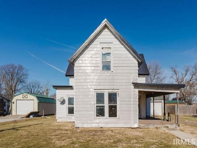 back of property with a garage, an outdoor structure, fence, and a lawn