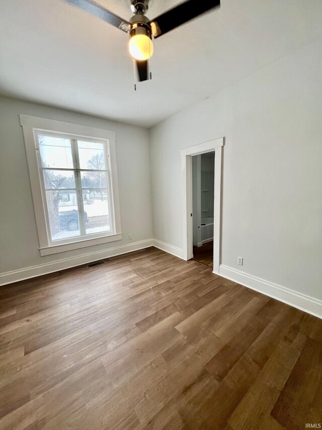 empty room featuring a ceiling fan, wood finished floors, visible vents, and baseboards