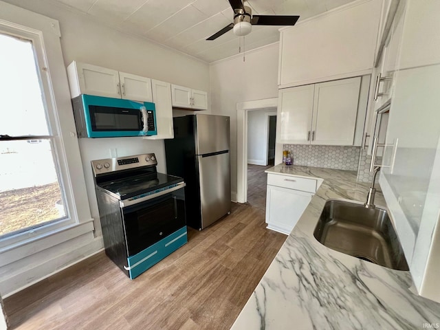 kitchen with appliances with stainless steel finishes, light wood-type flooring, white cabinets, and a sink