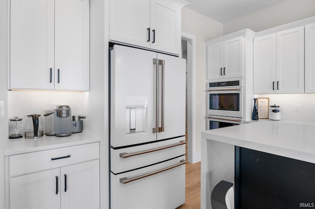 kitchen with light countertops, white appliances, light wood-type flooring, and white cabinetry