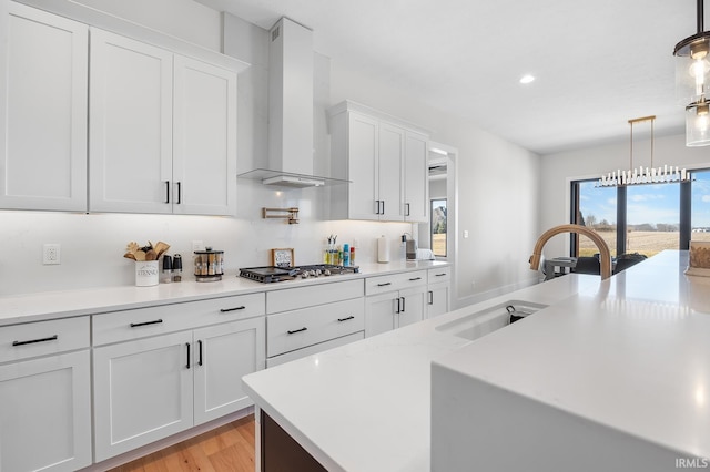 kitchen with wall chimney exhaust hood, a sink, decorative light fixtures, and white cabinets