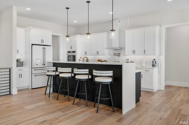 kitchen featuring high end white refrigerator, a kitchen island with sink, white cabinetry, and light countertops