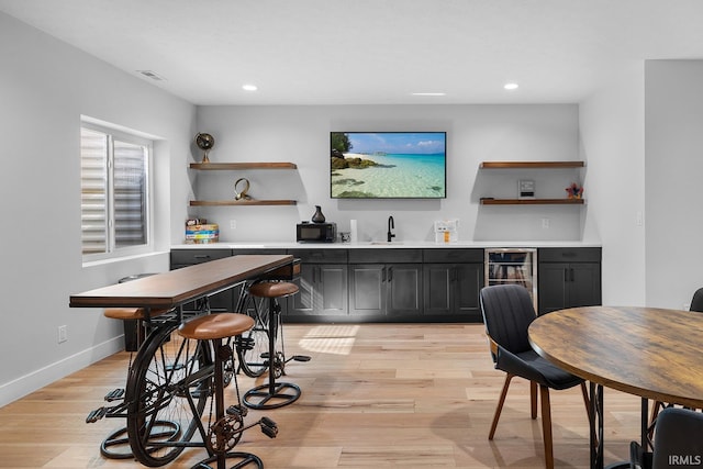 bar featuring beverage cooler, visible vents, baseboards, wet bar, and light wood finished floors