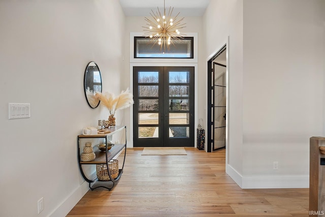 foyer entrance with baseboards, french doors, an inviting chandelier, and light wood-style floors