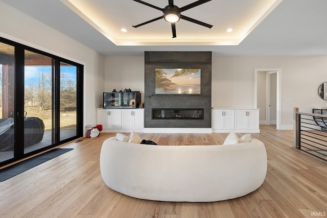 living room featuring a large fireplace, light wood-style flooring, a raised ceiling, and recessed lighting