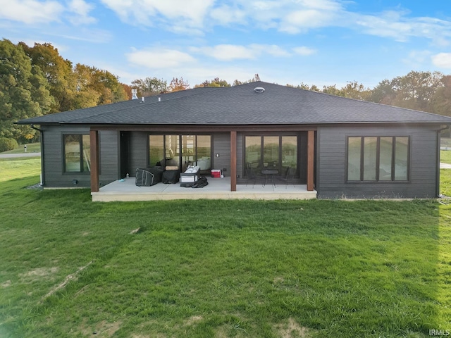 rear view of house featuring a shingled roof, a patio area, and a lawn