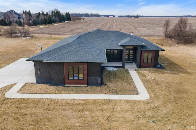 view of front of home featuring a shingled roof, a front yard, a rural view, and brick siding