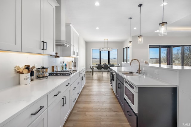 kitchen featuring decorative light fixtures, appliances with stainless steel finishes, light wood-style floors, white cabinets, and a sink