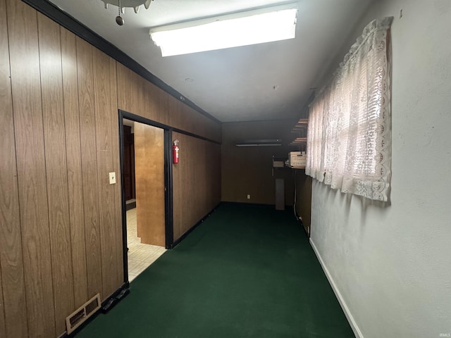 hall featuring dark carpet, visible vents, and wooden walls