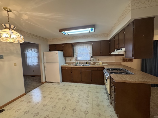 kitchen with hanging light fixtures, freestanding refrigerator, gas stove, a sink, and under cabinet range hood