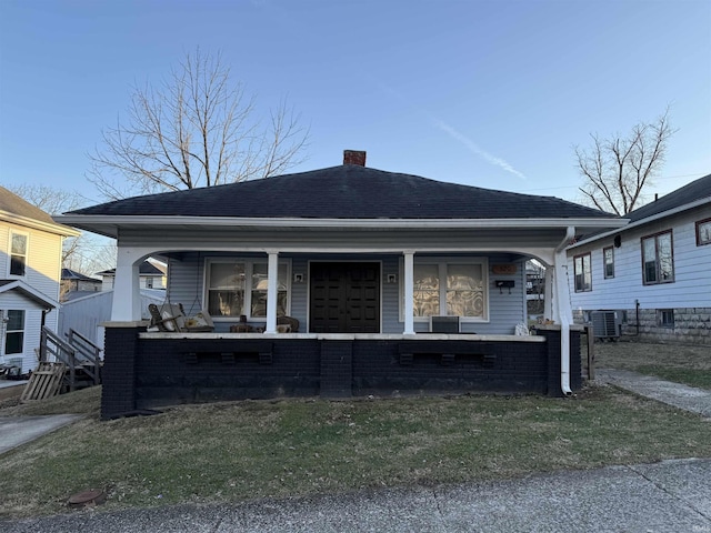 bungalow with central air condition unit, covered porch, a chimney, and roof with shingles