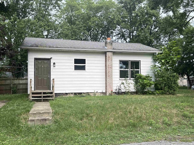 view of front of home with entry steps, a chimney, fence, and a front lawn