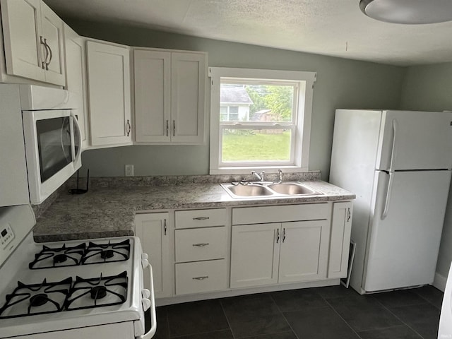 kitchen featuring white appliances, dark tile patterned floors, a sink, and white cabinets