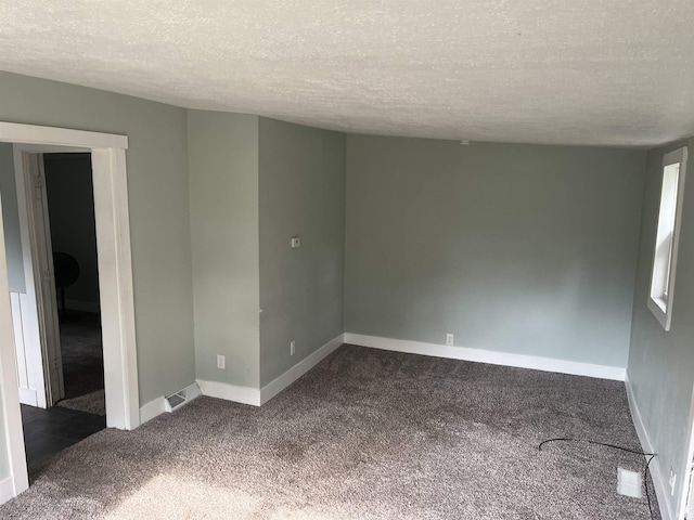 spare room featuring a textured ceiling, dark colored carpet, visible vents, and baseboards