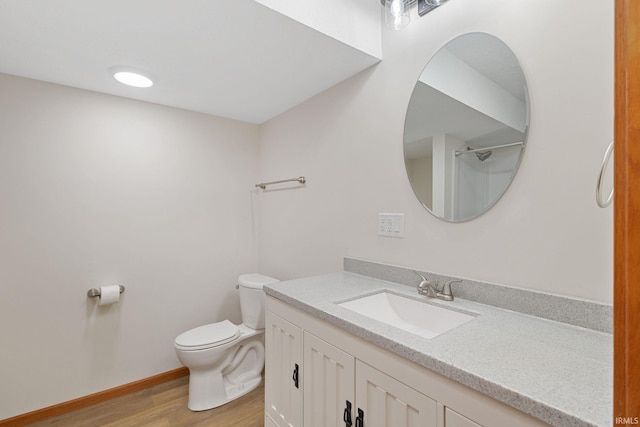 bathroom with toilet, wood finished floors, vanity, baseboards, and walk in shower