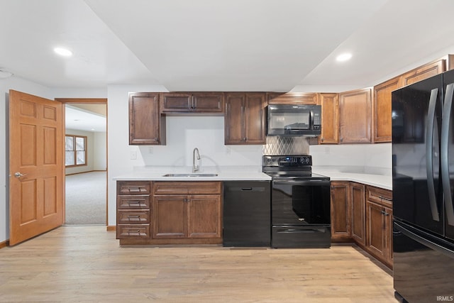 kitchen with a sink, black appliances, light wood finished floors, and light countertops