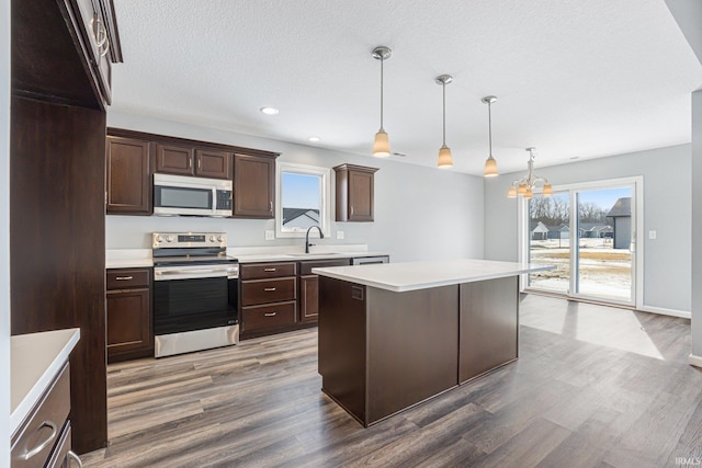 kitchen featuring a center island, pendant lighting, light countertops, appliances with stainless steel finishes, and dark brown cabinetry