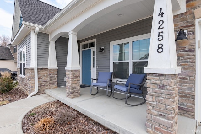 doorway to property with a porch, stone siding, and roof with shingles