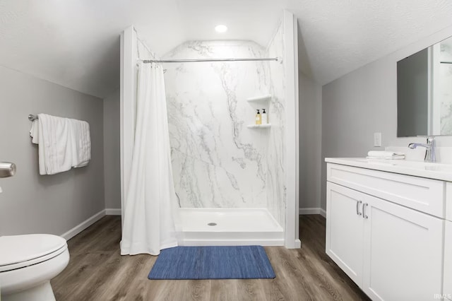 bathroom featuring toilet, wood finished floors, vanity, vaulted ceiling, and a stall shower