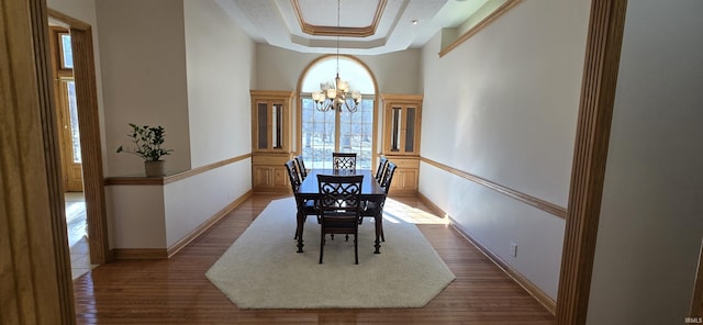 dining area with an inviting chandelier, baseboards, a tray ceiling, and wood finished floors