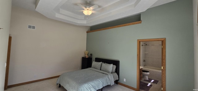 bedroom featuring light carpet, visible vents, baseboards, a raised ceiling, and ensuite bath